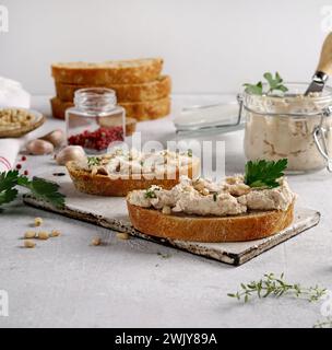 Pâté maison, tartinade ou mousse dans un pot en verre avec du pain tranché et des herbes, fond de béton léger. Banque D'Images