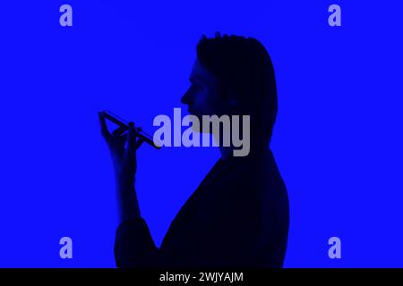 Silhouette un homme d'affaires élégant parlant sur un téléphone portable dans une veste debout sur un fond bleu brillant, concepts futuristes d'IA Banque D'Images