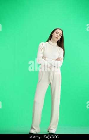 Une femme, pleine longueur, sur un fond vert, croisa les bras Banque D'Images