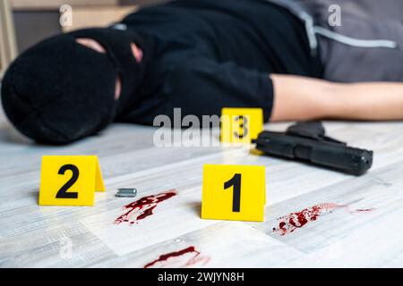 Augsbourg, Bavière, Allemagne - 16 février 2024 : image symbolique scène de crime posée scène. Un cambrioleur masqué est mort sur le sol à côté d'un pistolet et d'une douille de cartouche marquée avec des marques de preuve de la police *** Symbolbild Kriminal Szene gestellte Szene. Ein Maskierter Einbrecher liegt tot auf dem Boden neben einer Pistole und einer Patronenhülse markiert mit Beweismittel Markierungen der Polzei Banque D'Images