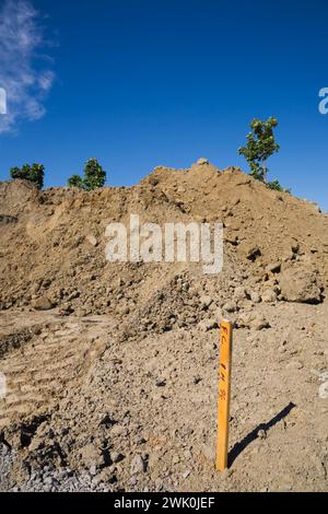 Piquet d'arpenteur en bois peint en orange dans un sol brun clair sur le chantier de construction. Banque D'Images