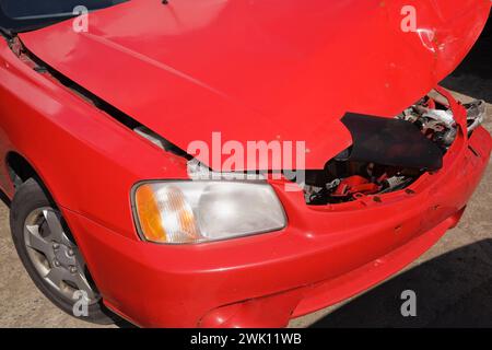 Gros plan d'une voiture rouge avec un pneu crevé et un capot de compartiment moteur endommagé causé par une collision frontale. Banque D'Images