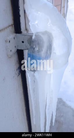 Un cadenas sur une porte métallique à l'extérieur d'un bâtiment, couvert de glace. Inconvénients hivernaux. Banque D'Images