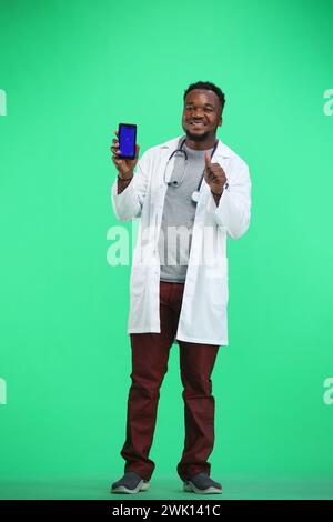 Le médecin, en pleine hauteur, sur fond vert, montre le téléphone Banque D'Images