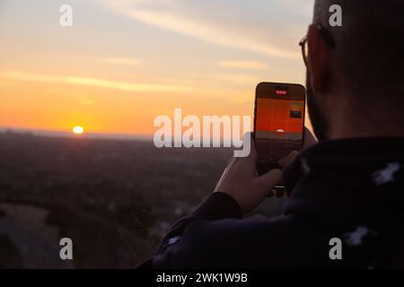 Un homme prenant une photo du coucher de soleil sur son téléphone de Baldwin Hills Overlook, Los Angeles, CA, USA Banque D'Images