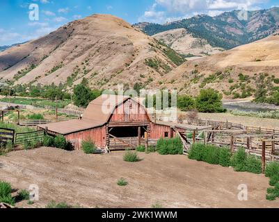 Un ranch rural près de Lucile, Idaho comprend une grange rouge classique et un corral de bois à côté de la rivière Salmon inférieure et des montagnes. Banque D'Images