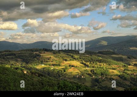 Maisons dispersées dans la belle campagne dans la lumière et l'ombre sous les nuages spectaculaires près d'Ivanjica, dans le sud-ouest de la Serbie Banque D'Images