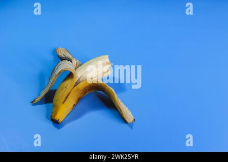 une banane avec une tête mordue sur un fond bleu faisant le contraste Banque D'Images