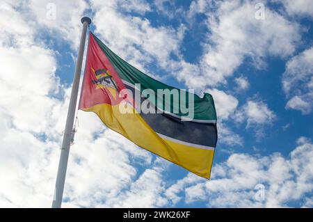 Drapeau du Mozambique agitant au vent. Drapeau national de la République du Mozambique. Drapeau avec fusil Kalachnikov et houe, superposé sur un livre ouvert. Banque D'Images
