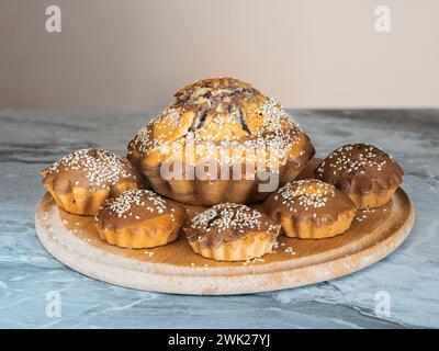 Muffins fraîchement cuits saupoudrés de graines de sésame sur une planche à découper ronde en bois de hêtre Banque D'Images