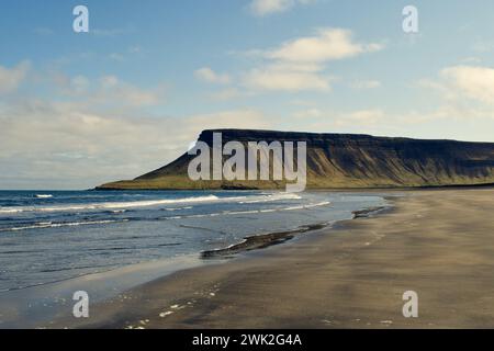 Plage de sable noir avec des rochers et des réflexes en rocade en Islande avec falaises, océan et herbe verte pendant une journée ensoleillée Banque D'Images