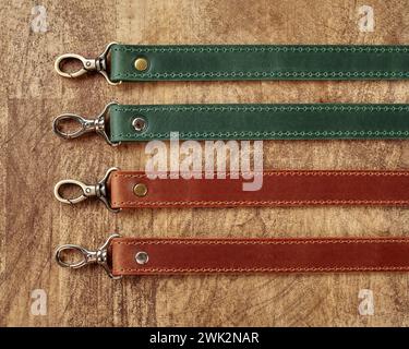 Collection de sangles de sac en cuir de différentes couleurs avec des mousquetons métalliques sur fond en bois, mettant en valeur l'utilité et l'artisanat Banque D'Images