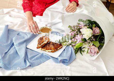 Élégant cadre romantique du matin avec femme en rouge appréciant le petit déjeuner au lit avec des croissants au chocolat français frais remplis de crème anglaise délicate et t Banque D'Images