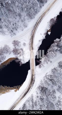 Saison d'hiver vue aérienne de haut en bas d'un pont, route d'hiver enneigée traversant la forêt couverte de neige en Suède Banque D'Images