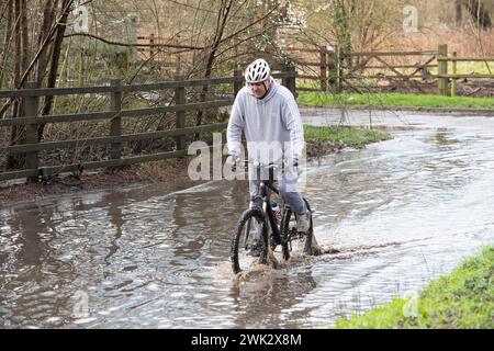 Eton, Windsor, Royaume-Uni. 18 février 2024. Un cycliste traverse les eaux de crue sur un pays à Eton, Windsor, Berkshire après de fortes pluies nocturnes. Crédit : Maureen McLean/Alamy Live News Banque D'Images