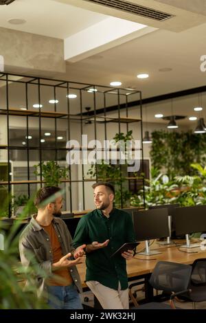 Deux professionnels sont engagés dans une conversation ciblée tout en tenant une tablette numérique dans un espace de bureau contemporain, avec brickwor exposé rustique Banque D'Images