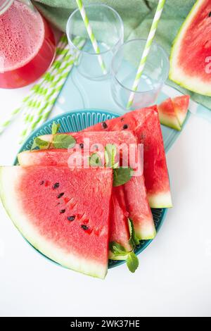 Tranches de pastèque fraîche sur une assiette bleue, garnies de menthe, à côté d’un smoothie rafraîchissant et de fruits entiers Banque D'Images