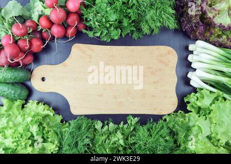 Divers légumes, légumes verts frais et épices et planche à découper vide. Ingrédients colorés pour cuisiner sur une table en bois rustique autour de bo de découpe vide Banque D'Images