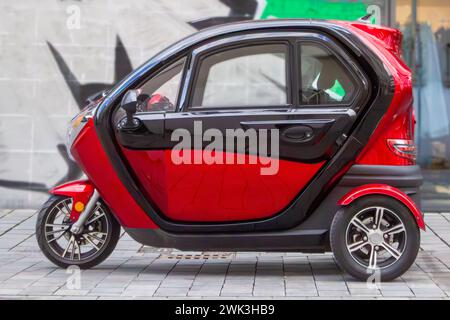 une voiture rouge à trois roues sur le fond d'un mur peint Banque D'Images