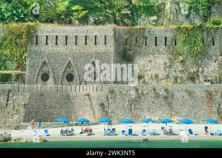 Vue sur la mer depuis la mer Tyrrhénienne et le golfe de Salerne, partie de la zone du patrimoine de l'UNESCO d'Amalfi les gens se relaxent autour de chaises longues et parasols bleus sur la plage privée au sommet de la falaise hors de l'image cinq étoiles Borgo Santandrea hôtel avec toile de fond de vieilles fortifications très près de la ville d'Amalfi Campanie sud de l'Italie dans une image d'archive historique. Banque D'Images