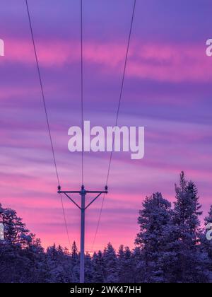 Cette image capture la beauté sereine d'un lever de soleil hivernal avec des cieux violets et roses vibrants, silhouette par des arbres chargés de neige et les lignes sombres de E. Banque D'Images