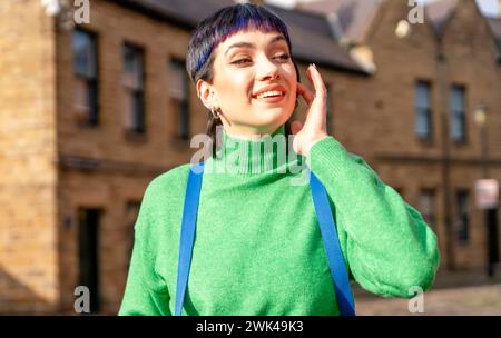 Une joyeuse jeune femme en vacances. Un touriste avec un sac à dos, vêtu d'un pull vert se promène dans une vieille ville européenne en vacances. Banque D'Images