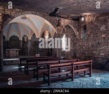 Rangées de bancs d'église, monastère en falaise. Sant Miquel del FAI est une photo de monastère bénédictin du XIe siècle. La lumière du soleil filtrée à travers la tache Banque D'Images