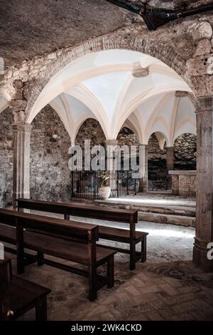 Rangées de bancs d'église, monastère en falaise. Sant Miquel del FAI est une photo de monastère bénédictin du XIe siècle. La lumière du soleil filtrée à travers la tache Banque D'Images