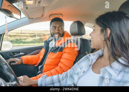 Beau jeune couple aimant heureux tenant la main et souriant tout en étant assis dans leur première voiture. Achetez votre première image tonifiée de concept de voiture Banque D'Images