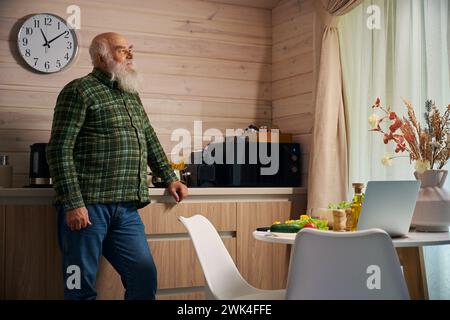 Vieil homme dans une chemise à carreaux chaude se tient dans la cuisine Banque D'Images