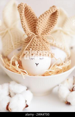 Oeufs de Pâques dans des chapeaux tricotés au crochet avec des oreilles de lapin dans le nid. Concept de célébration de Pâques Banque D'Images