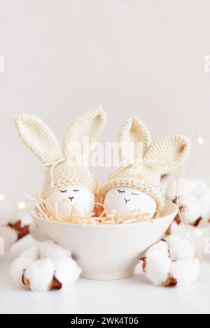 Oeufs de Pâques dans des chapeaux tricotés au crochet avec des oreilles de lapin dans le nid. Concept de célébration de Pâques Banque D'Images