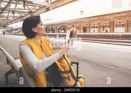 Jeune femme détenant passeport et billets, et attendant le train à la gare appréciant le concept de voyage Banque D'Images