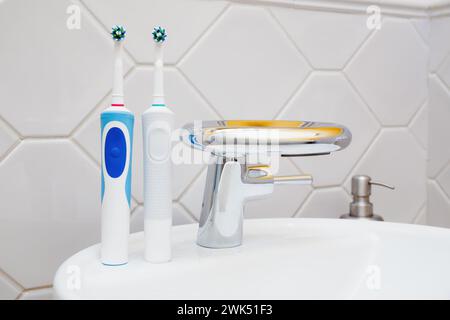 Deux brosses à dents électriques placées à côté, brosses à dents familiales, évier moderne avec robinet en rcéramique dans une salle de bain carrelée. Banque D'Images