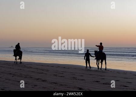 Cavaliers en silhouette sur une plage de sable au coucher du soleil à Essaouira, Maroc. 18 février 2024 Banque D'Images