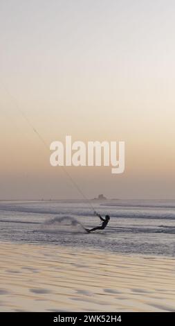 Kite surfer en silhouette au coucher du soleil avec affleurement rocheux à l'horizon à Essaouira, Maroc. 18 février 2024 Banque D'Images