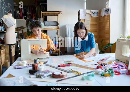 Vue de face portrait de deux jeunes filles cousant des vêtements tout en travaillant comme apprenties dans un atelier inclusif Banque D'Images