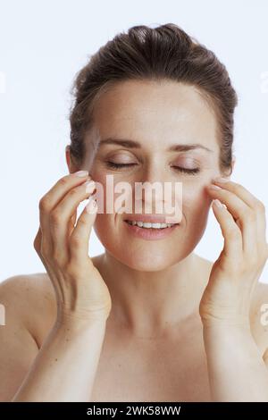 femme moderne heureuse faisant le massage facial sur fond blanc. Banque D'Images