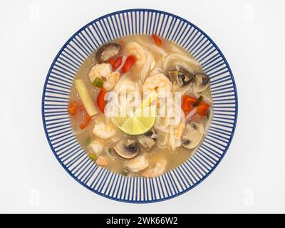 Offrez-vous un bol de soupe japonaise ramen, remplie de crevettes, champignons, tomates, citronnelle, et citron vert, servi dans un bol bleu et blanc sur un ba blanc Banque D'Images