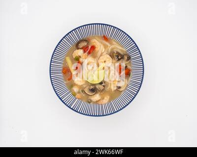 Offrez-vous un bol de soupe japonaise ramen, remplie de crevettes, champignons, tomates, citronnelle, et citron vert, servi dans un bol bleu et blanc sur un ba blanc Banque D'Images