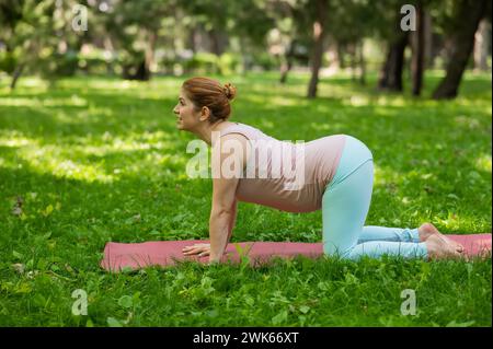 Femme blanche enceinte faisant du yoga dans le parc. Pose chat-vache. Banque D'Images