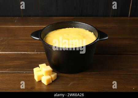 Casserole à fondue avec fromage fondu et morceaux à table en bois Banque D'Images