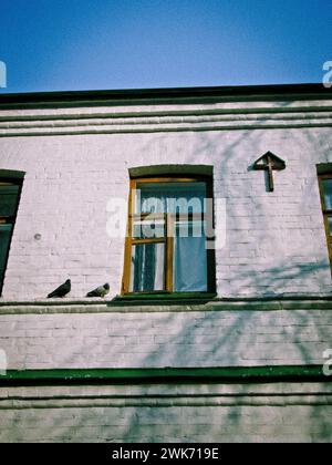 Une fenêtre dans un monastère orthodoxe, deux colombes sur la corniche, une croix accrochée à un mur blanc Banque D'Images