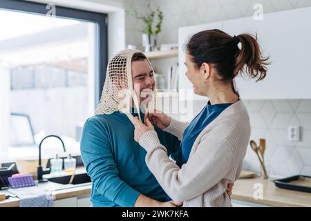 Jeune homme avec le syndrome de Down et sa mère étant drôle, ont un sac de filet de mash sur la tête. Conception de l'amour et de la parentalité de l'enfant handicapé. Banque D'Images