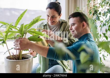 Vue de dessus d'un jeune homme atteint du syndrome de Down avec sa mère à la maison, prenant soin des plantes d'intérieur. Conception de l'amour et de la parentalité de l'enfant handicapé. Banque D'Images