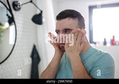 Jeune homme avec le syndrome de Down dans la salle de bain, tenant ses joues. Banque D'Images