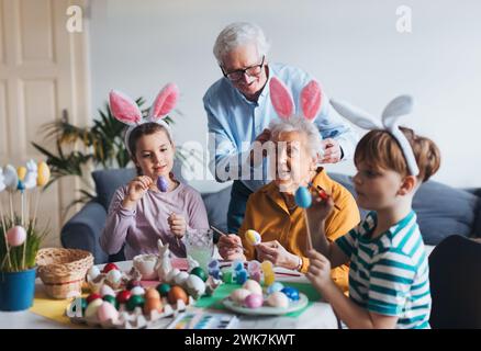 Grand-mère avec de petits enfants décorant des œufs de pâques à la maison. Tradition de peindre les oeufs avec pinceau et colorant d'oeuf de pâques. Banque D'Images