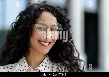 Jeune femme d'affaires hispanique aux cheveux bouclés profitant d'une pause déjeuner à l'extérieur de son bureau, rayonnant de professionnalisme et de joie. Banque D'Images