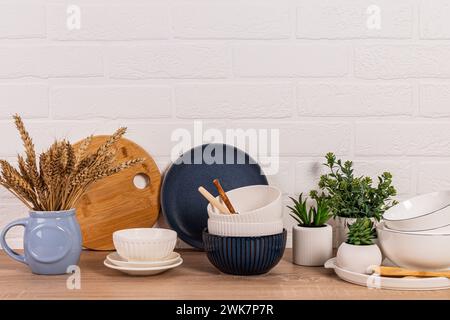 Beau fond de cuisine avec différents bols en céramique, plantes d'intérieur en pot. Vue de face. Mur de briques blanches Banque D'Images