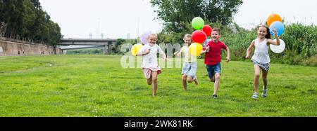 Les enfants avec des ballons courent dans le parc d'été Banque D'Images